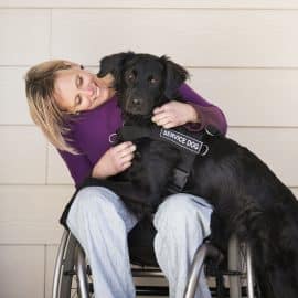 A wheelchair user with her service assistance dog, a black labrador whose front paws are on her lap.