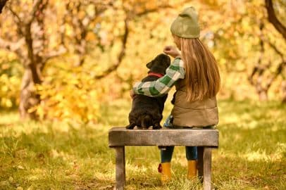 A girl sitting on the bench with her dog in the park