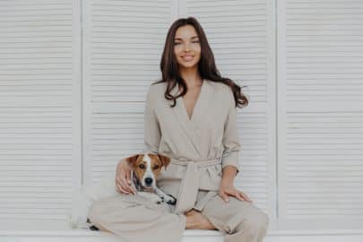 Elegant woman in chic attire with her loyal dog, posing against a white shuttered backdrop